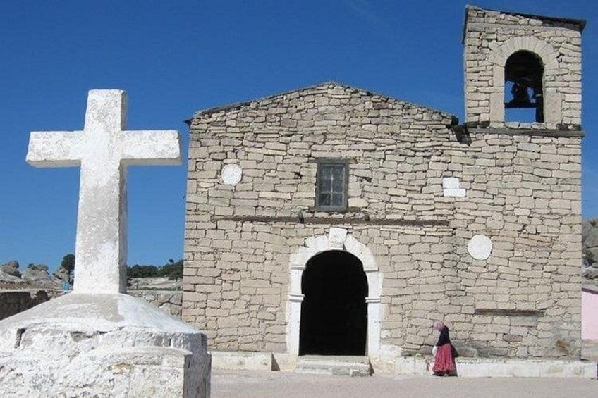 A stone church with a bell tower and a large white cross in front. 3