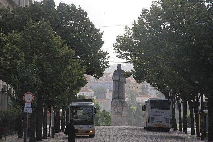 A street with two buses, a statue, and trees. 3
