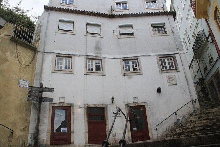 A multi-story building with red doors and windows, a staircase, and a signpost. 2
