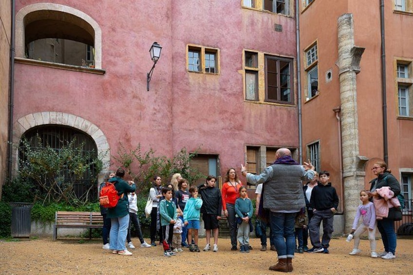 Eine Gruppe von Menschen steht vor einem rosafarbenen Gebäude mit einer Steinsäule und einer Bank im Hintergrund. 1