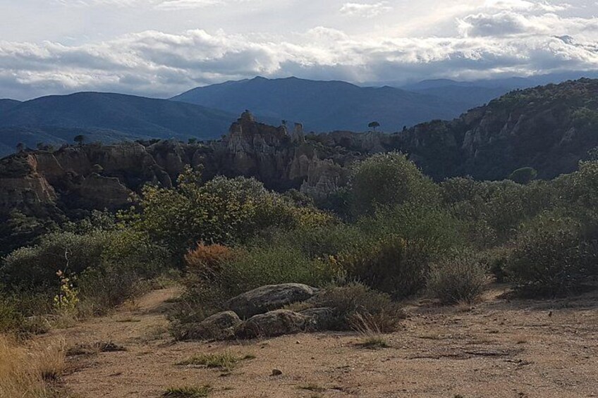 A rugged landscape with rocky outcrops, sparse vegetation, and distant mountains under a cloudy sky. 3