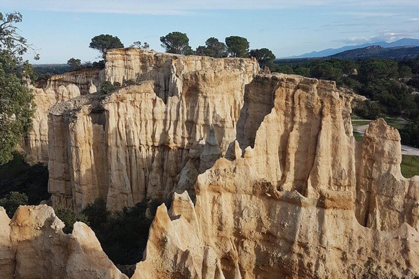 A limestone cliff formation with trees on top and a road in the background. 4