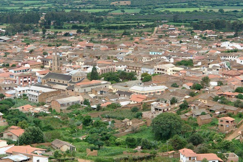 A densely packed town with numerous buildings, a prominent church, and surrounding green fields. 1