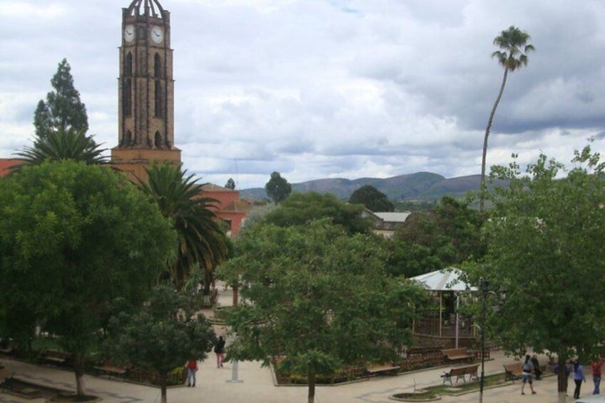 A clock tower, trees, and a park with people walking. 3