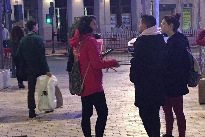 Personas de pie sobre un pavimento de ladrillo de noche, con una farola y semáforos al fondo. 2