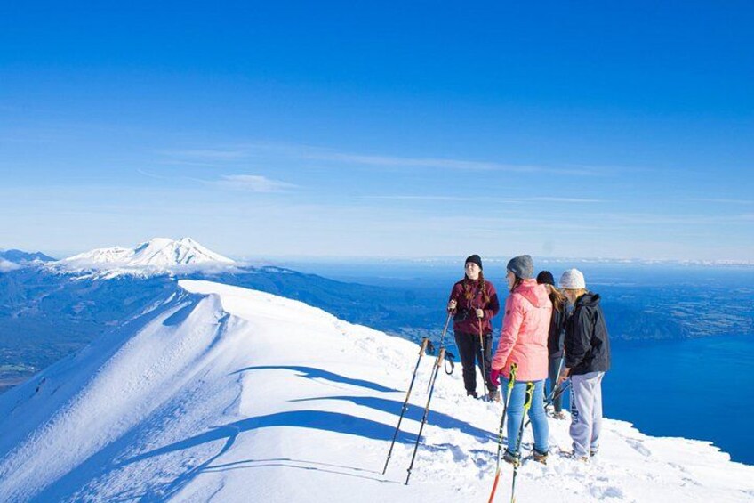 Een groep skiërs op een besneeuwde bergtop, met een heldere lucht en een bergketen in de verte. 3