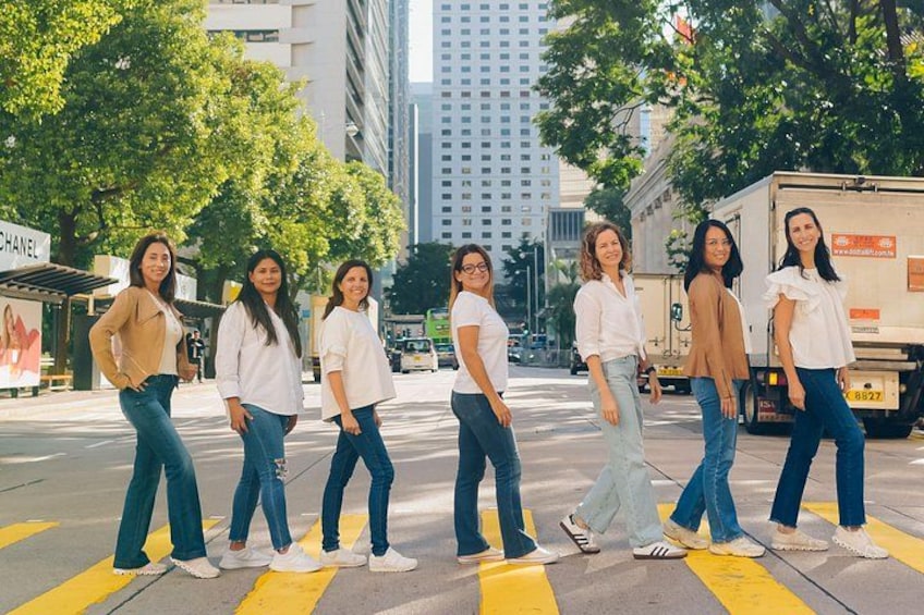A group of people standing on a crosswalk in an urban setting with tall buildings and trees in the background. 3
