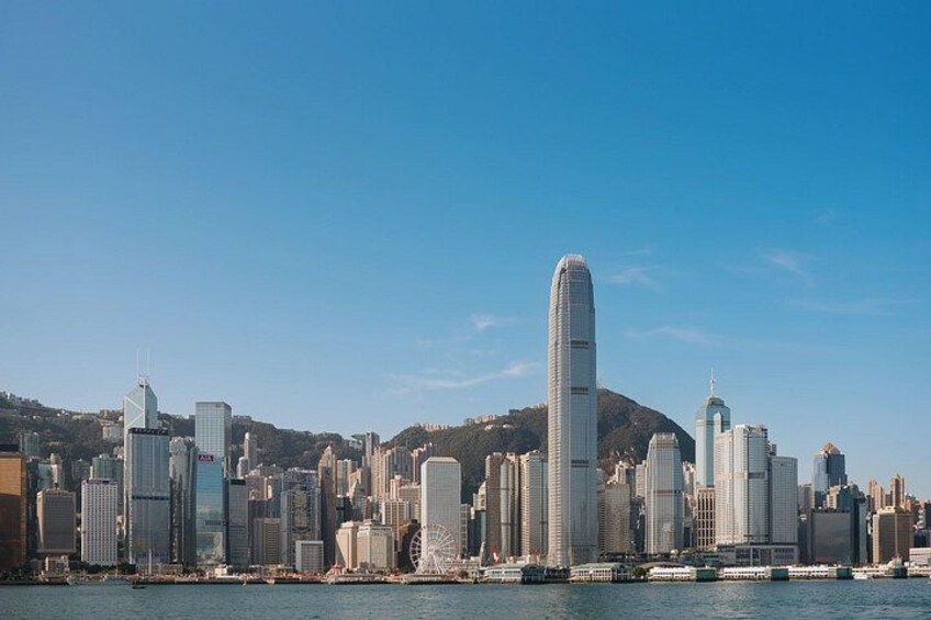 A city skyline with modern skyscrapers, a prominent cylindrical building, and a body of water in the foreground. 2