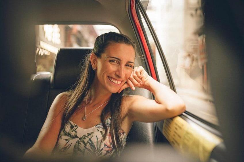 A person sitting in a car, wearing a floral dress, with a city street visible through the window. 1