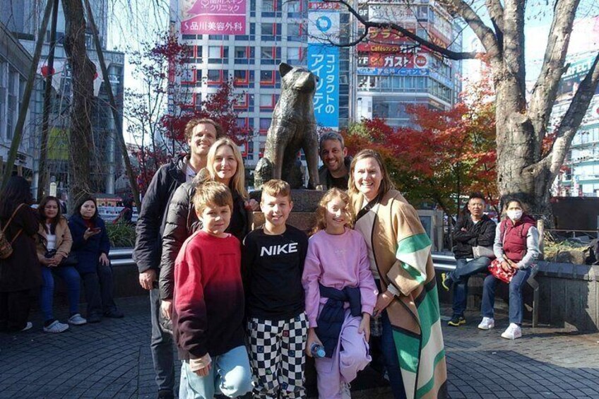 Een groep mensen poseert voor een standbeeld, met gebouwen en bomen op de achtergrond. 3
