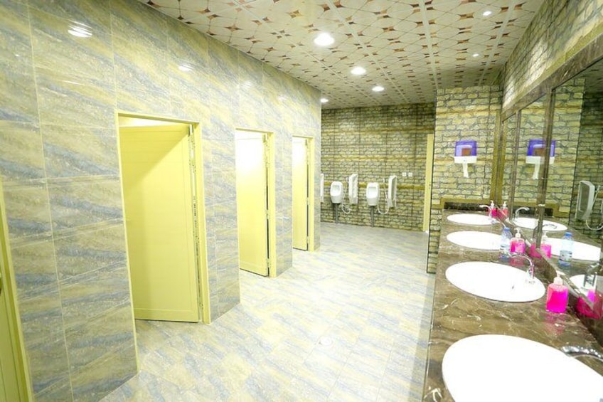 Un bagno pubblico con pareti in marmo, porte gialle e numerosi lavandini con specchi. 5