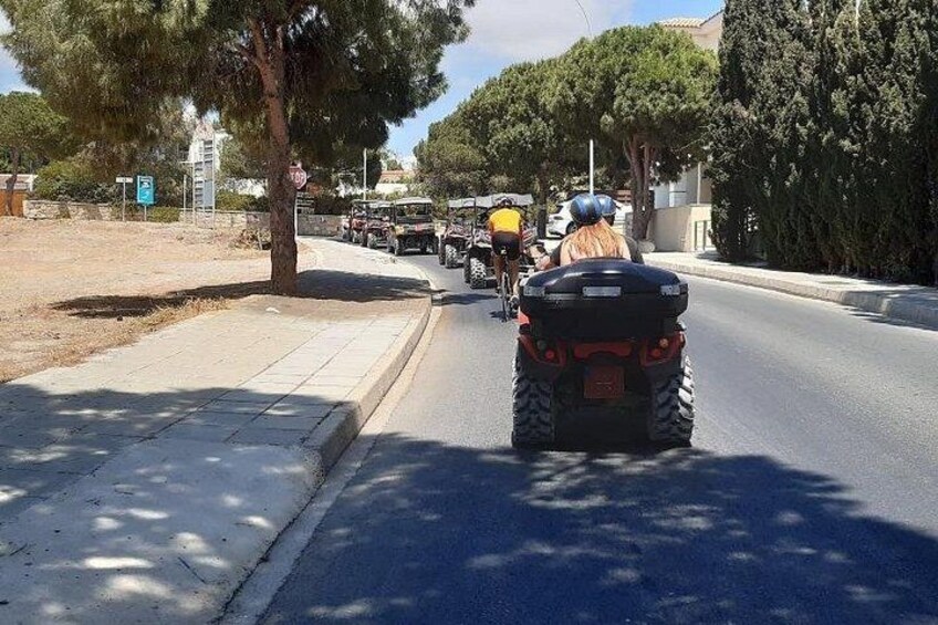 Una strada con una persona che guida un quad, un ciclista e un veicolo sullo sfondo. 2