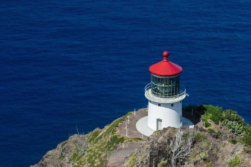 Un faro con la parte superior roja, ubicado en una costa rocosa con el océano al fondo. 4