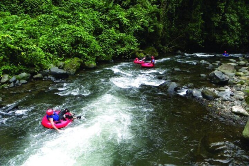 Two people rafting down a river surrounded by lush greenery. 2