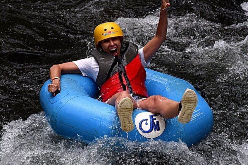A person in a blue inflatable raft with a helmet and life jacket, navigating through rapids. 1