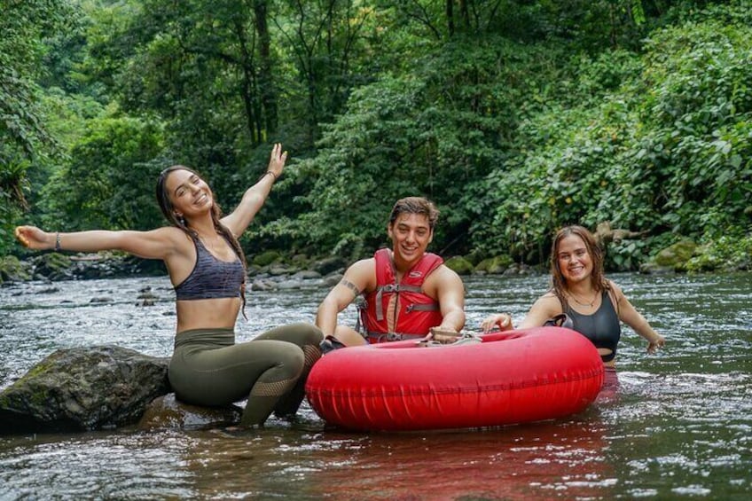 Three people on a red inflatable raft in a river surrounded by dense greenery. 3