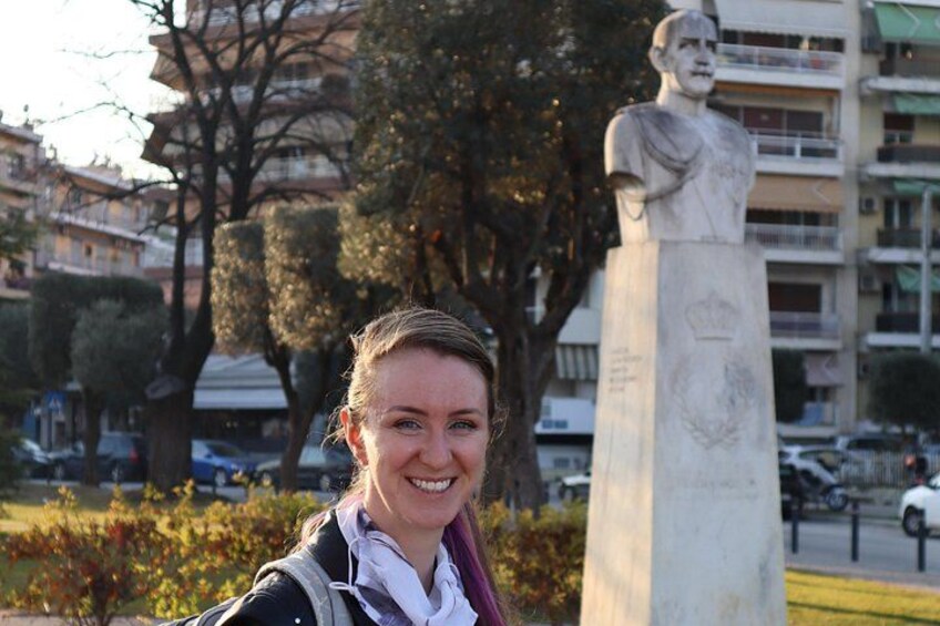 A person standing in front of a statue in a park with trees and buildings in the background. 5