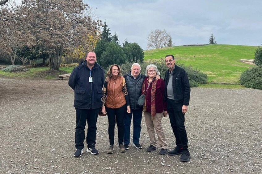 A group of people standing on a gravel path with trees and a grassy hill in the background. 4