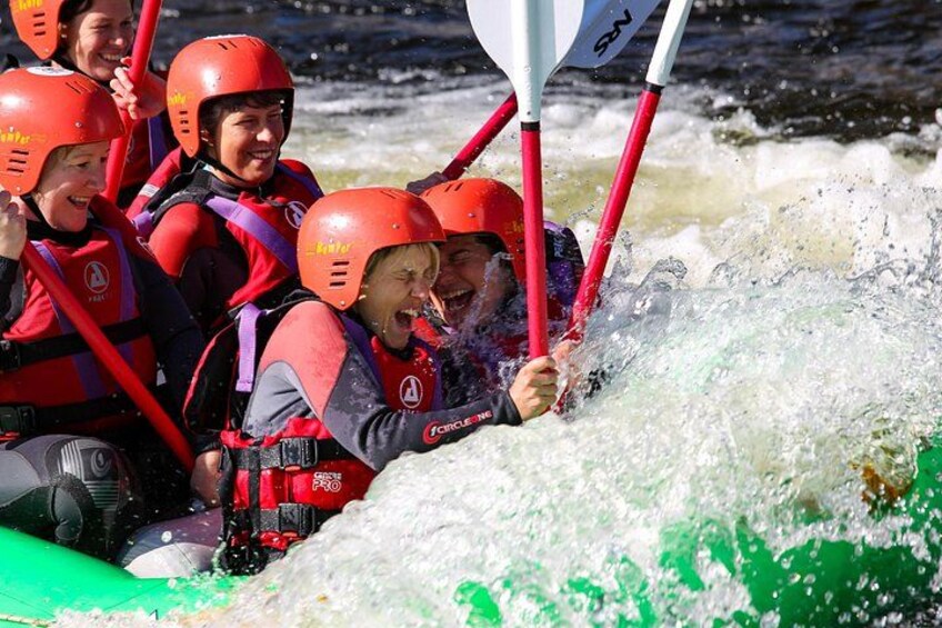 People in red helmets and life vests on a white raft navigating a river. 4