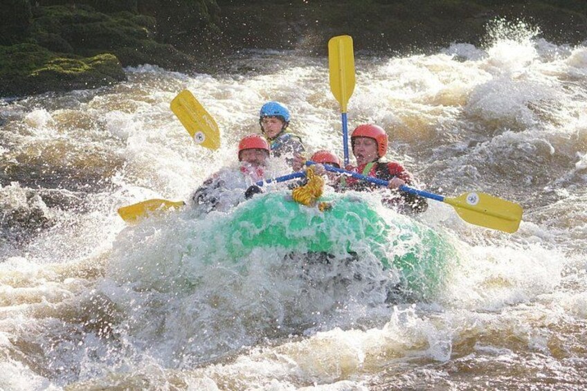 A group of people in a green inflatable raft navigating through whitewater rapids. 3