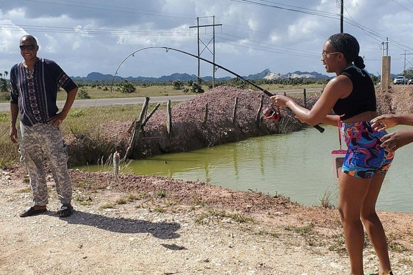 Two people fishing by a small body of water with a fence and power lines in the background. 3