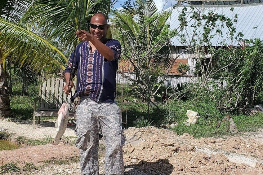 A person standing outdoors, holding a fish, with palm trees and a building in the background. 5
