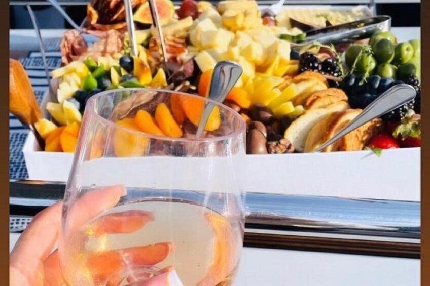 A glass of white wine, a charcuterie board with various cheeses, fruits, and bread. 3