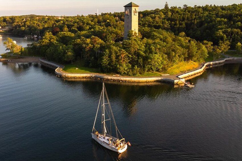 A sailboat on calm water near a forested island with a tower. 1