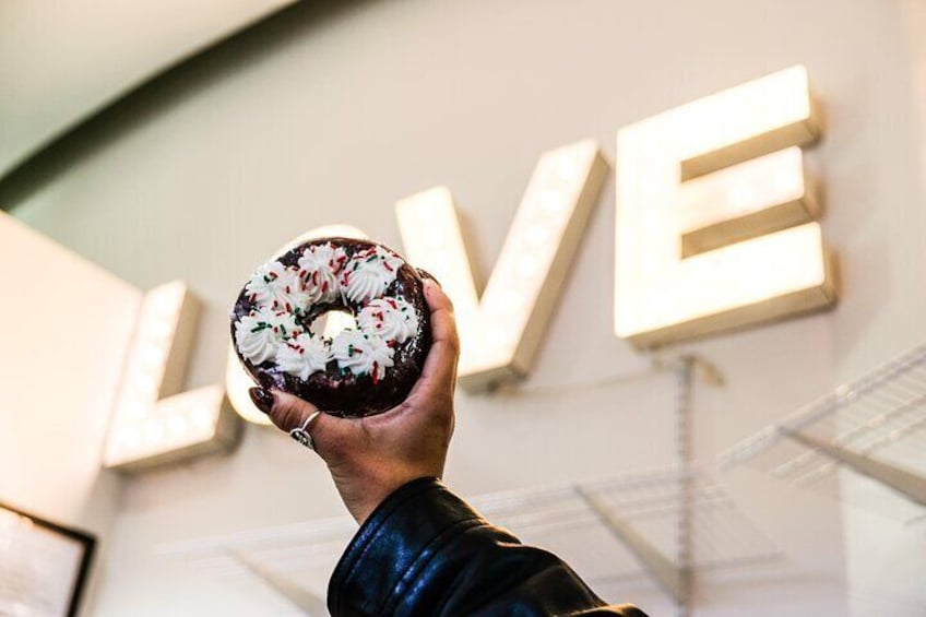 Eine Hand hält einen Schokoladendoughnut mit weißem und rotem Zuckerstreusel. 2