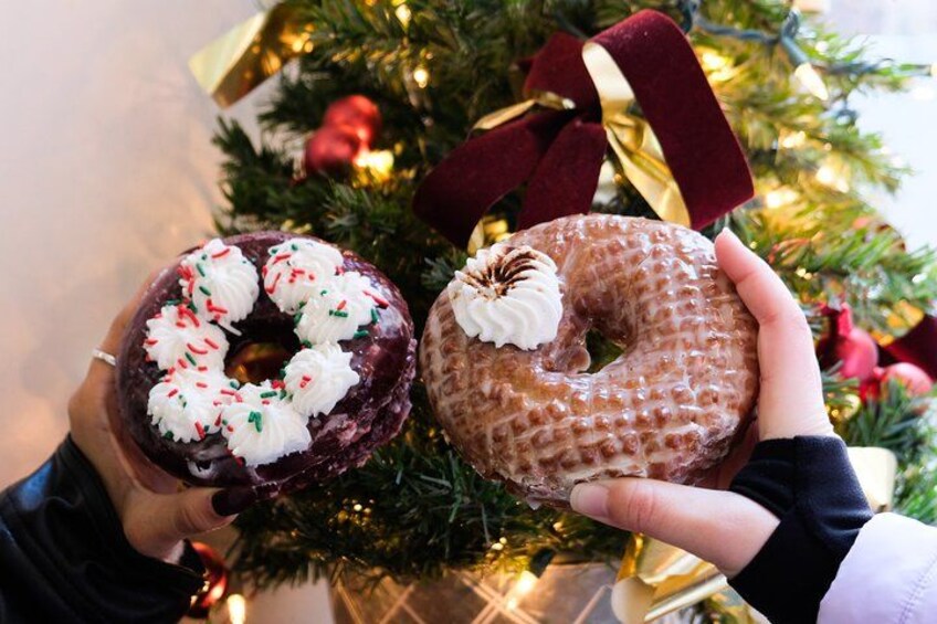 Two people holding donuts in front of a decorated Christmas tree. 2