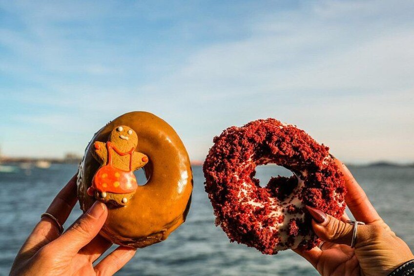 To hænder holder om en donut dækket med chokolade, med en peberkagefigur, og en red velvet donut med hvid frosting. 3