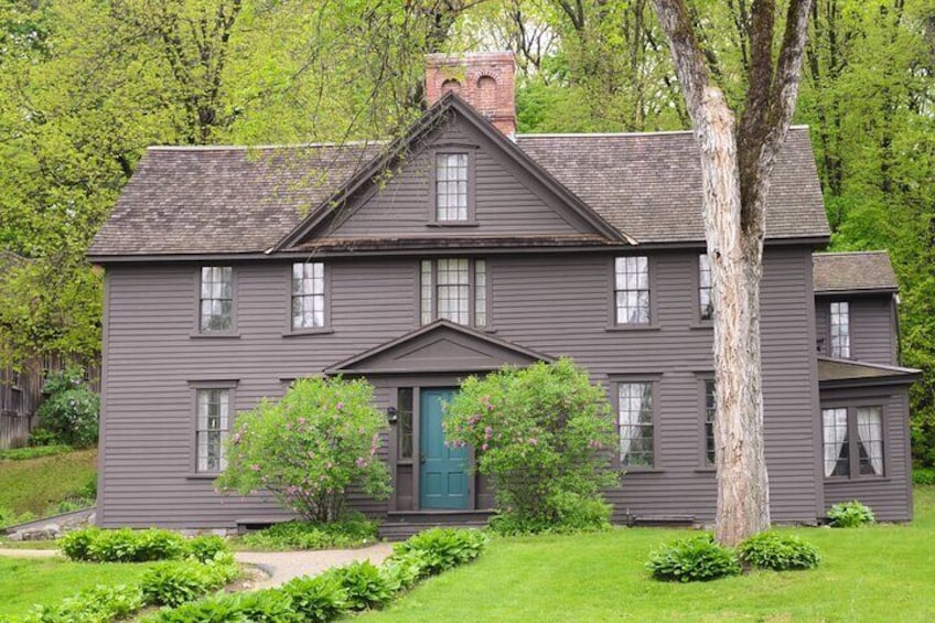 A two-story gray house with a green door, surrounded by lush greenery and trees. 5