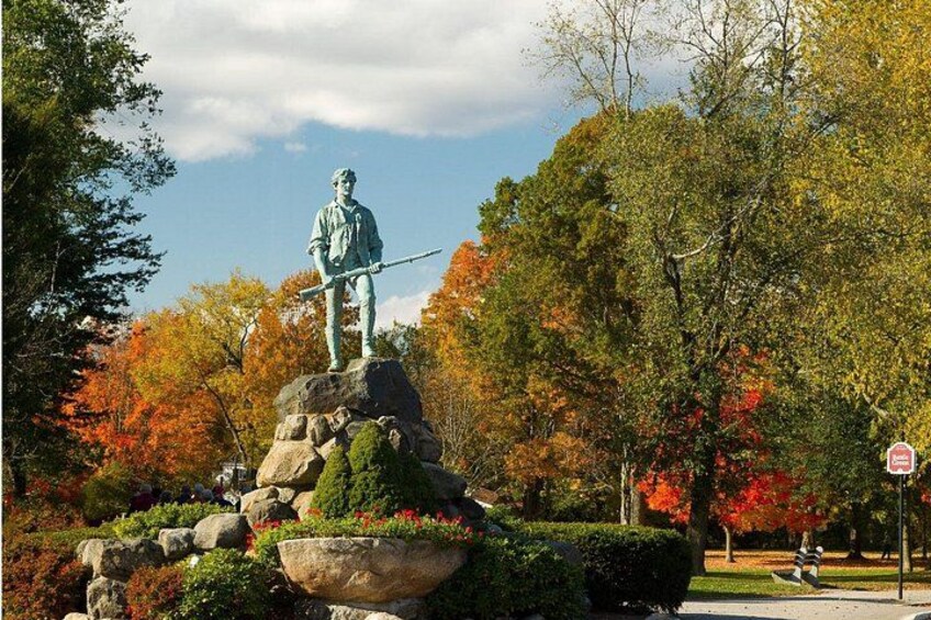 A statue of a figure holding a rifle, surrounded by autumn foliage and a stone planter. 1