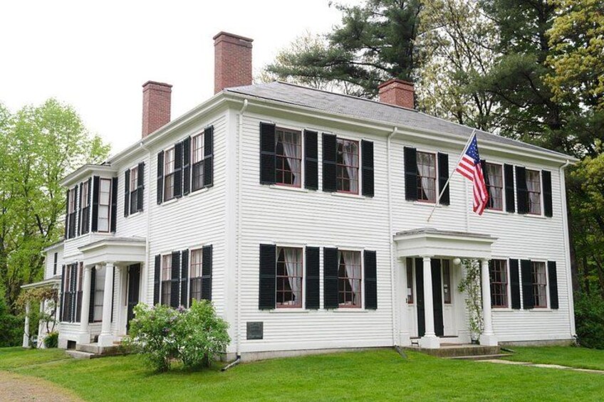 A white two-story house with black shutters, a brick chimney, and an American flag. 5