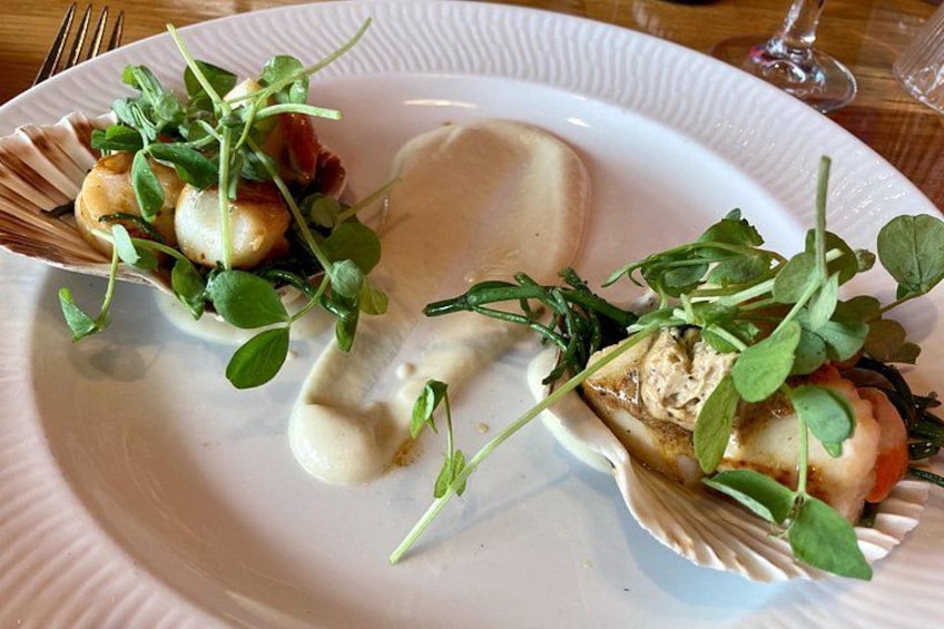 A plate with two scallops, greens, and a creamy sauce. 1