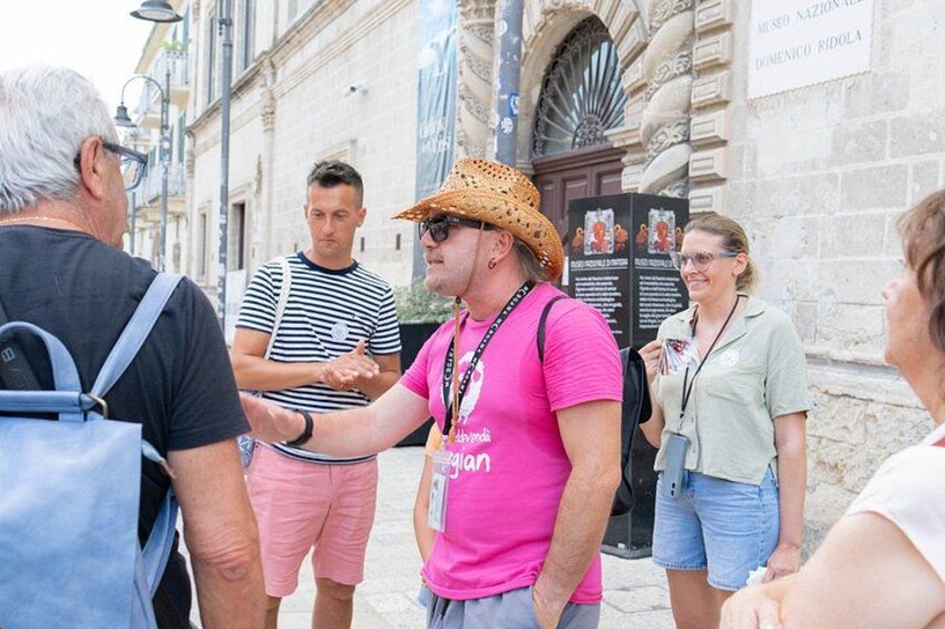 A group of people standing on a street with a stone building in the background. 3