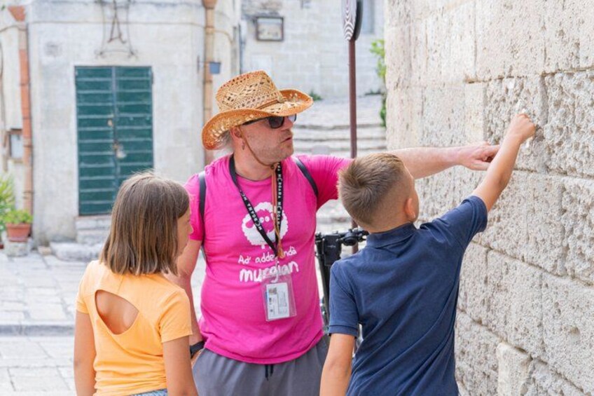 A person in a straw hat and pink shirt pointing at a stone wall. 4