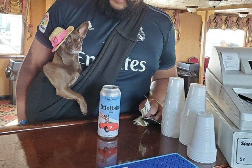 A person holding a small dog wearing a hat, a can of beer, and several plastic cups on a counter. 4