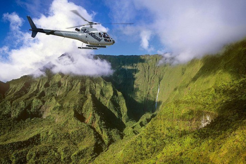 A helicopter flying over a lush green valley with a waterfall. 4
