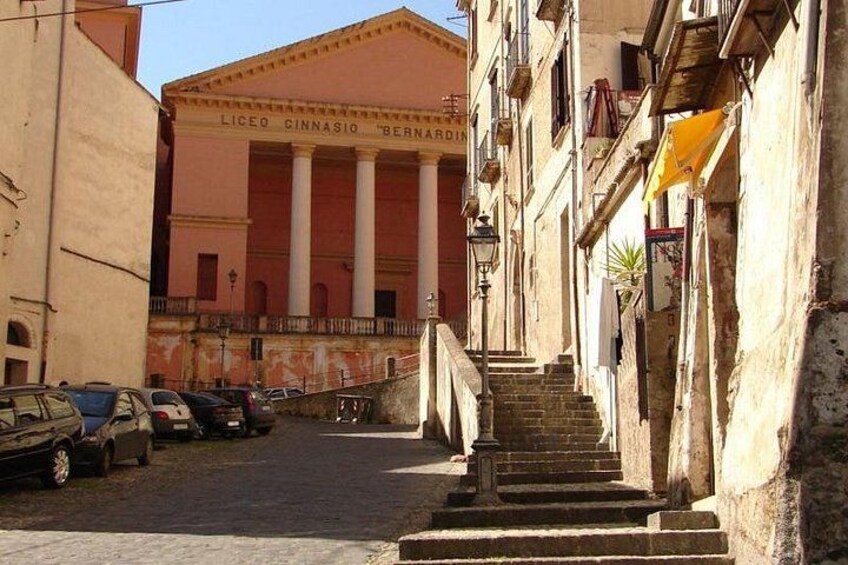 A street with parked cars, a building with columns, and a staircase leading up to a door. 2