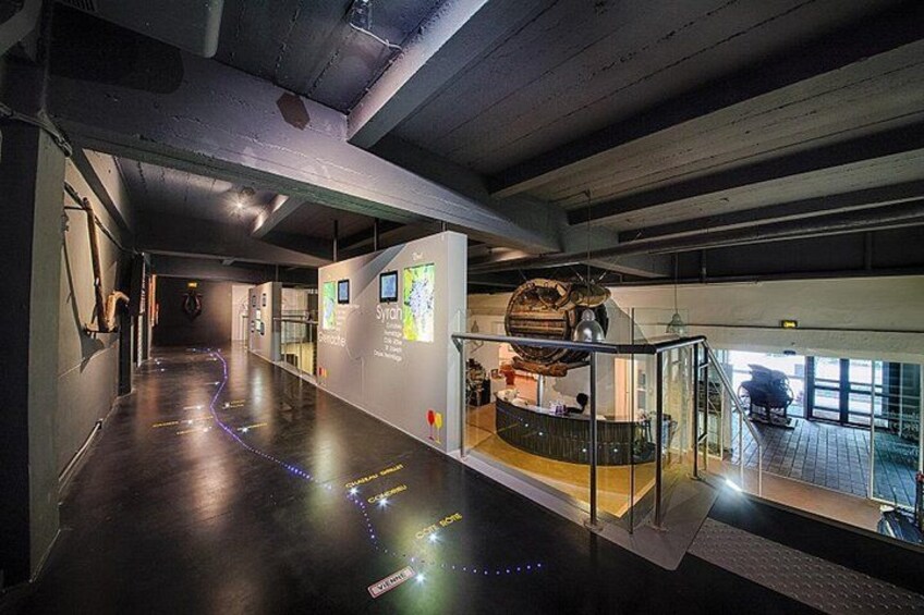 Un espace d’exposition intérieur comprenant un long couloir, des vitrines et des panneaux d’information. 2