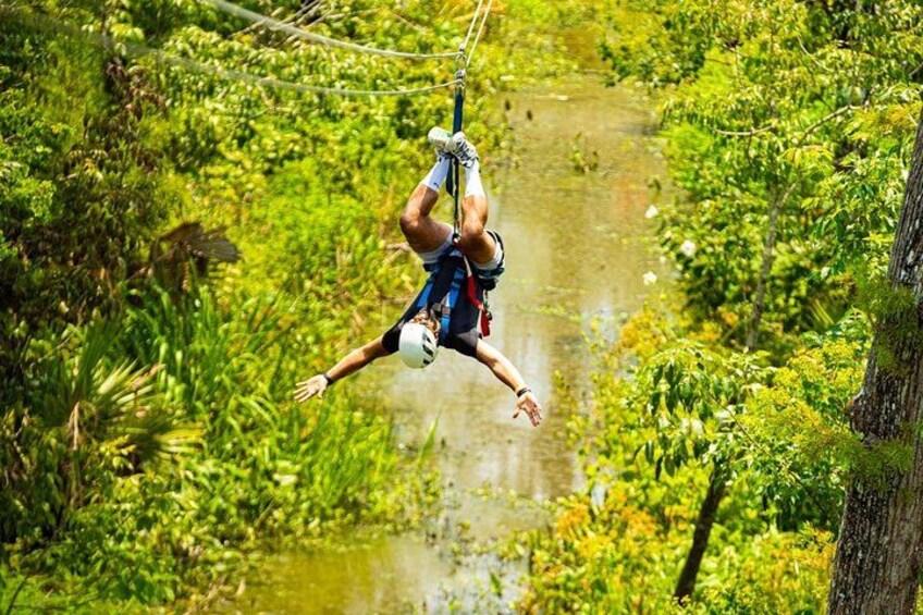 En person åker på en zipline genom en frodig, grön skog med tät vegetation och en flod nedanför. 2