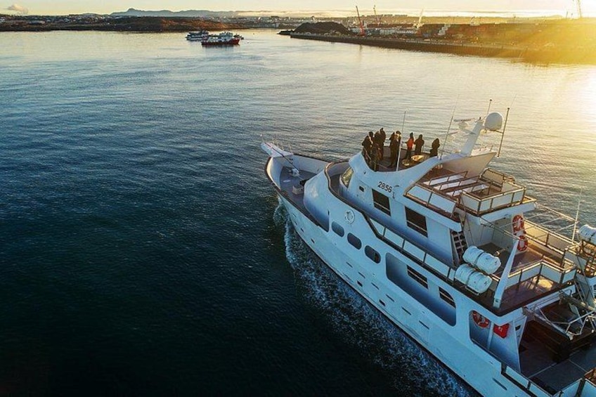 A white yacht with people on deck, docked at a harbor with calm water and a sunset in the background. 3