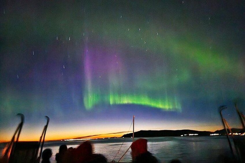 The Northern Lights over a body of water with a boat and people on the shore. 5