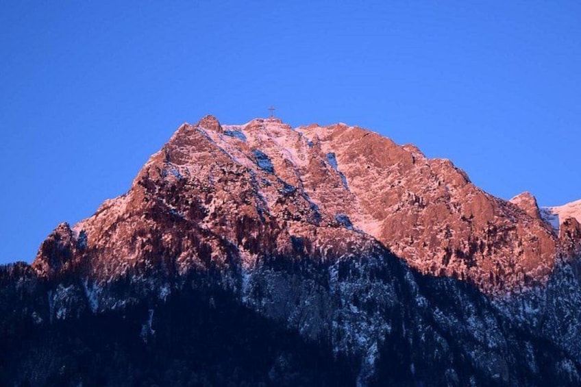 Una montaña con una cruz en la cima, terreno rocoso y un cielo azul despejado. 5