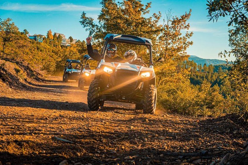 Two off-road vehicles on a dirt road surrounded by trees and hills. 1