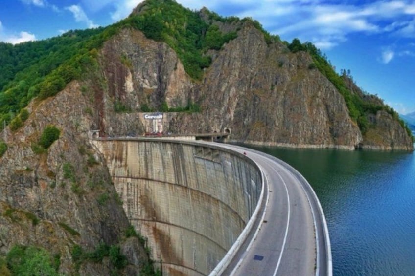 A dam with a road curving around it, a body of water, and a mountainous landscape. 4