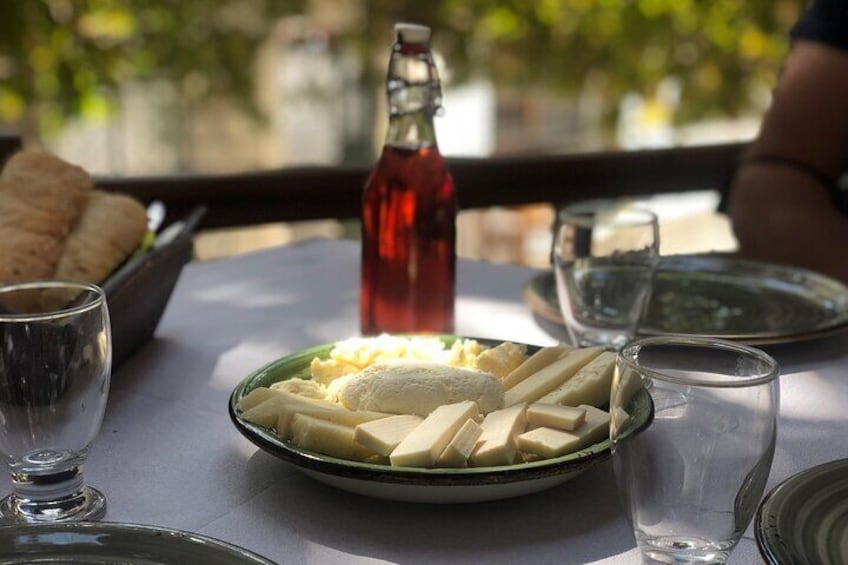 Una mesa con un plato de queso, una botella y vasos. 3