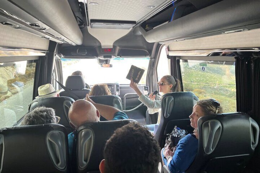 Interior de autobús con pasajeros sentados y un guía sosteniendo una tableta. 4