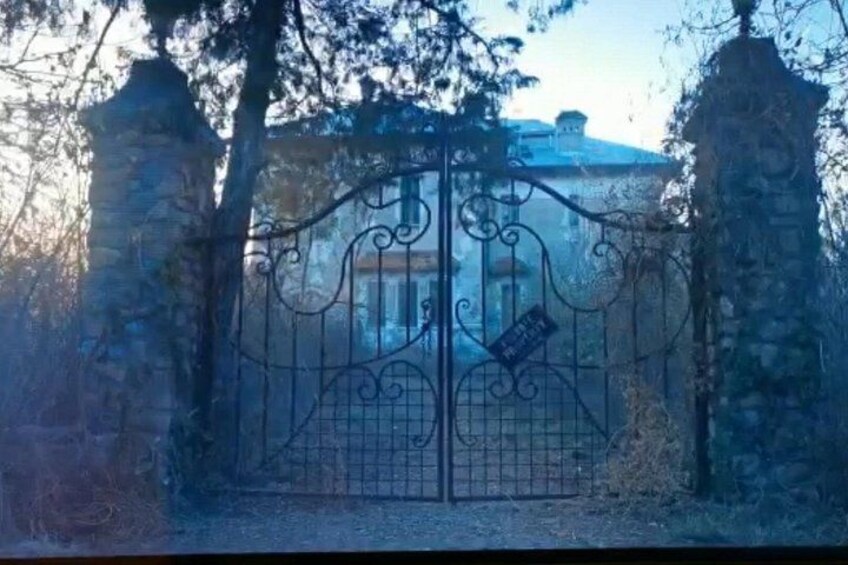 A wrought iron gate with a sign, flanked by stone pillars, leading to a building with a dome. 4